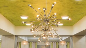 Um lustre moderno com vários braços e lâmpadas, pendurado em um teto com acabamento texturizado.
