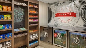 Exposição de petiscos com diferentes tipos de batatas fritas e lanches, uma lousa com desenhos rabiscados e uma geladeira com bebidas.