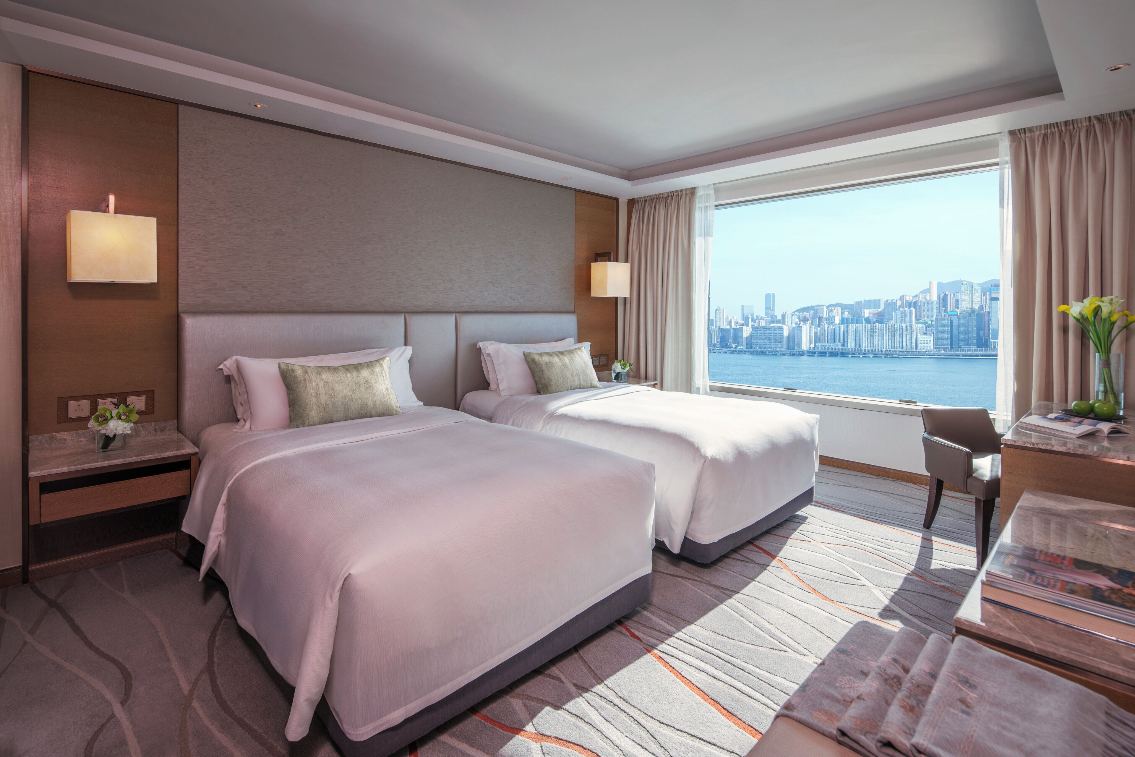 A hotel room with two beds, a desk, and a view of a city skyline.