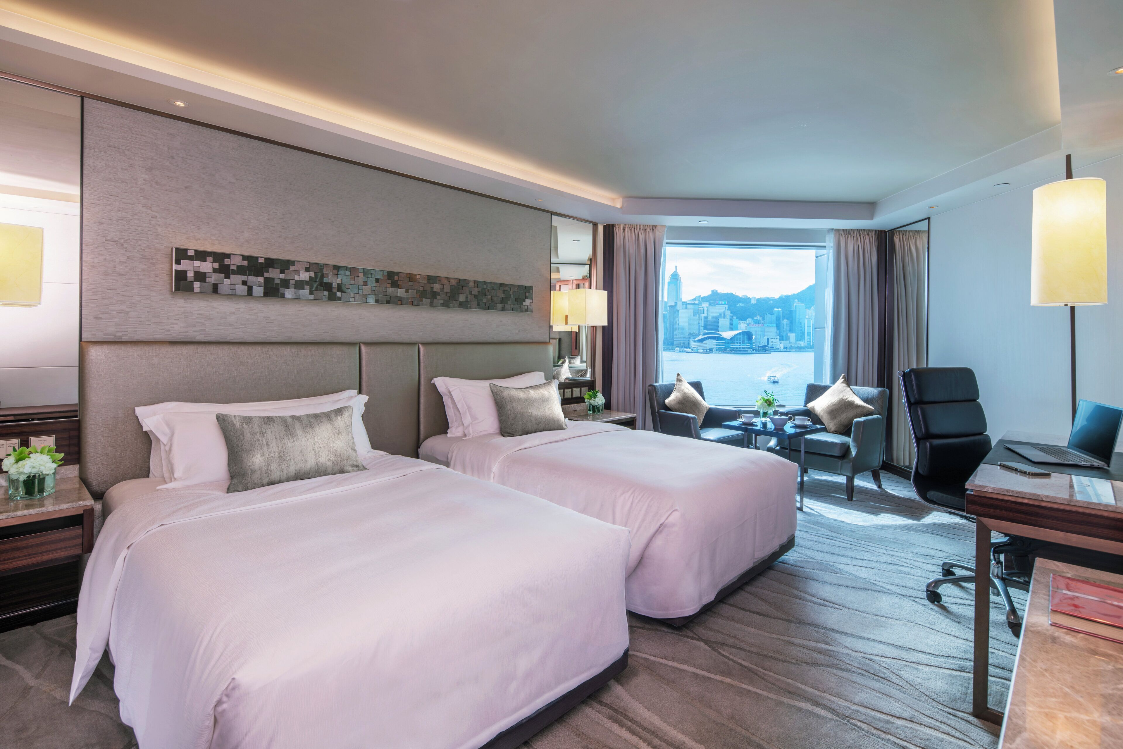 Habitación de hotel con dos camas, un escritorio, una silla y vistas a la ciudad.