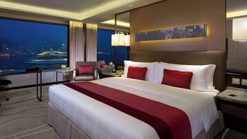 A hotel room with a large bed, a desk, a chair, a nightstand, and a view of the cityscape.