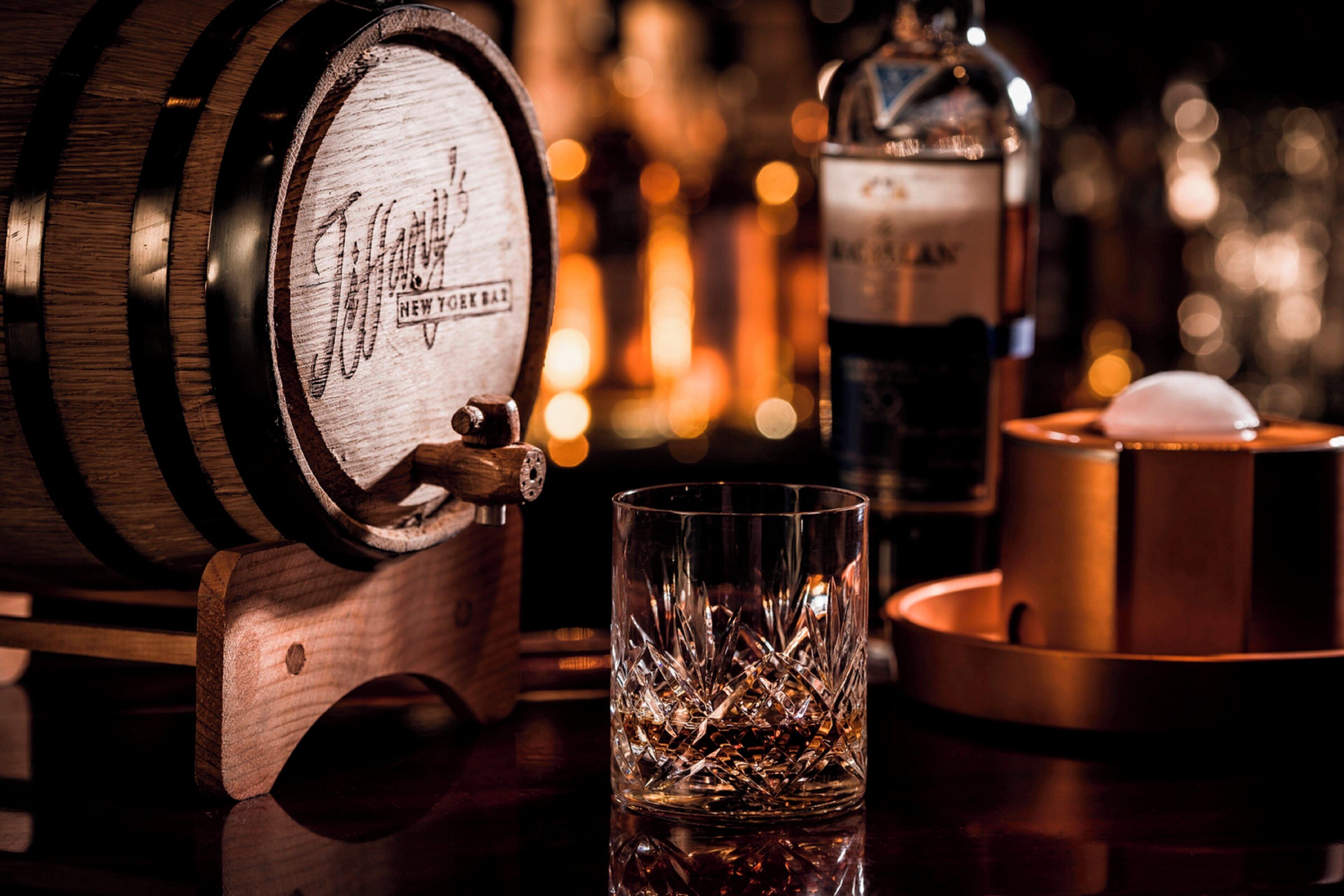 Un bar con un barril de madera, un vaso con hielo y una botella de licor.