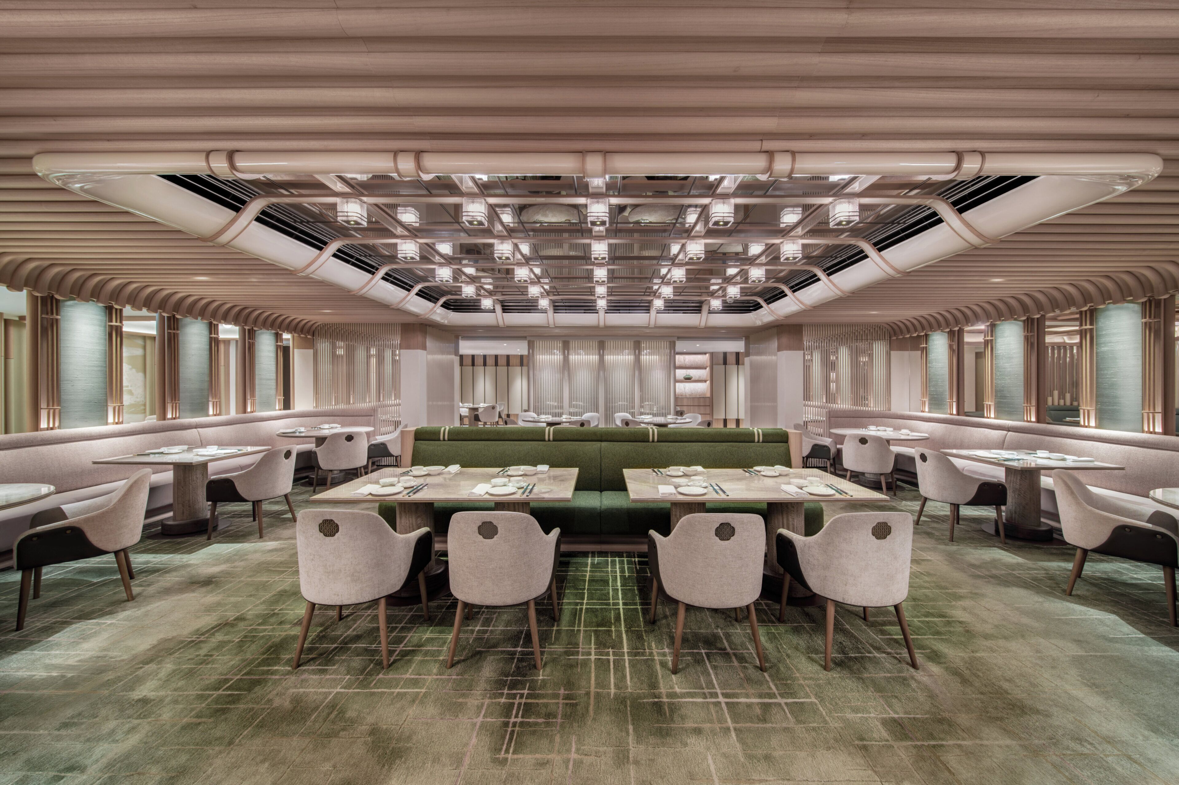 A spacious dining area with a long green table and multiple chairs, surrounded by large windows and a high ceiling with visible ductwork.