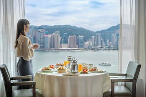 Une table à manger dressée avec des aliments pour le petit-déjeuner, offrant une vue sur le paysage urbain à travers de grandes fenêtres.