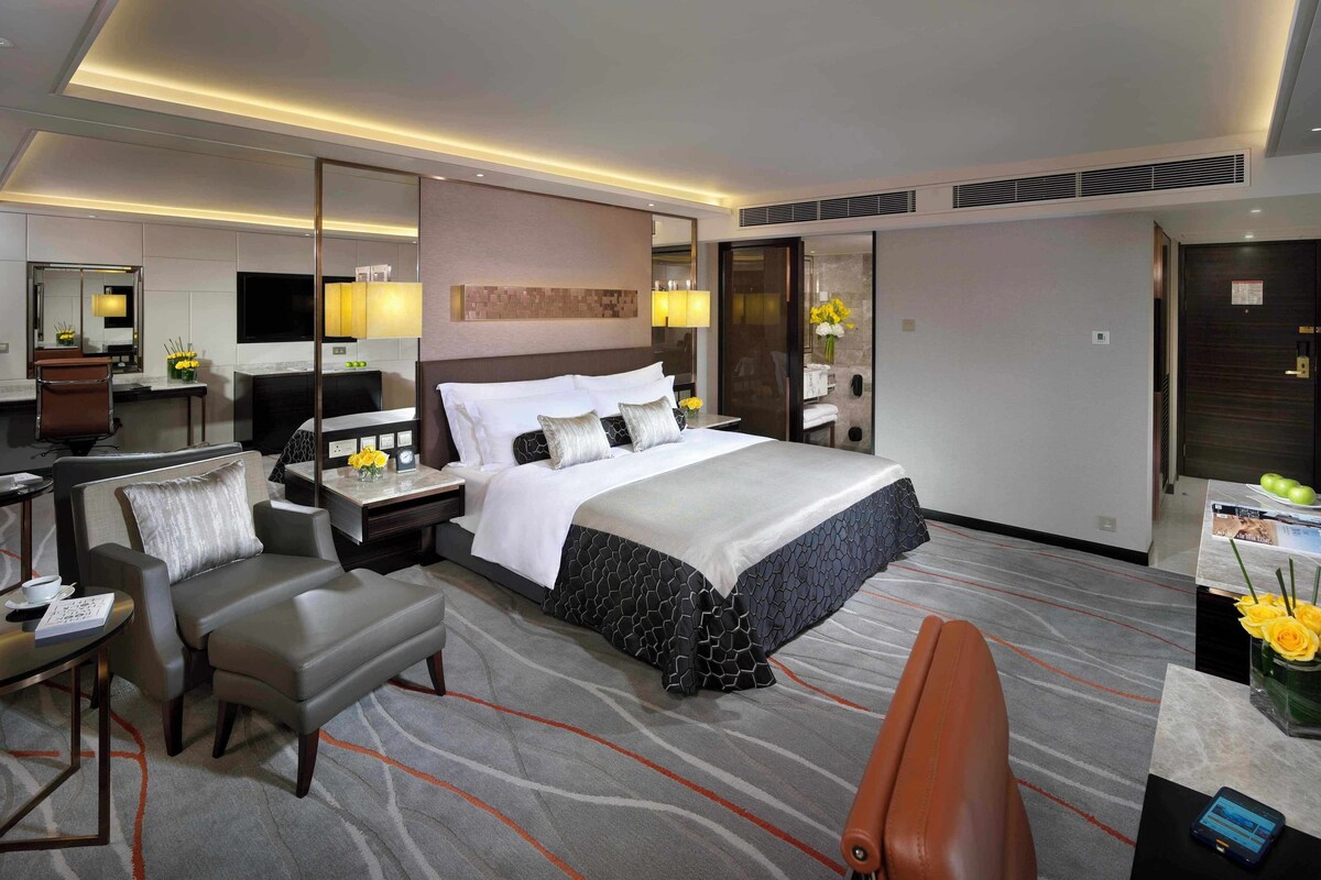 A modern hotel room with a large bed, a desk, a chair, and a sofa.