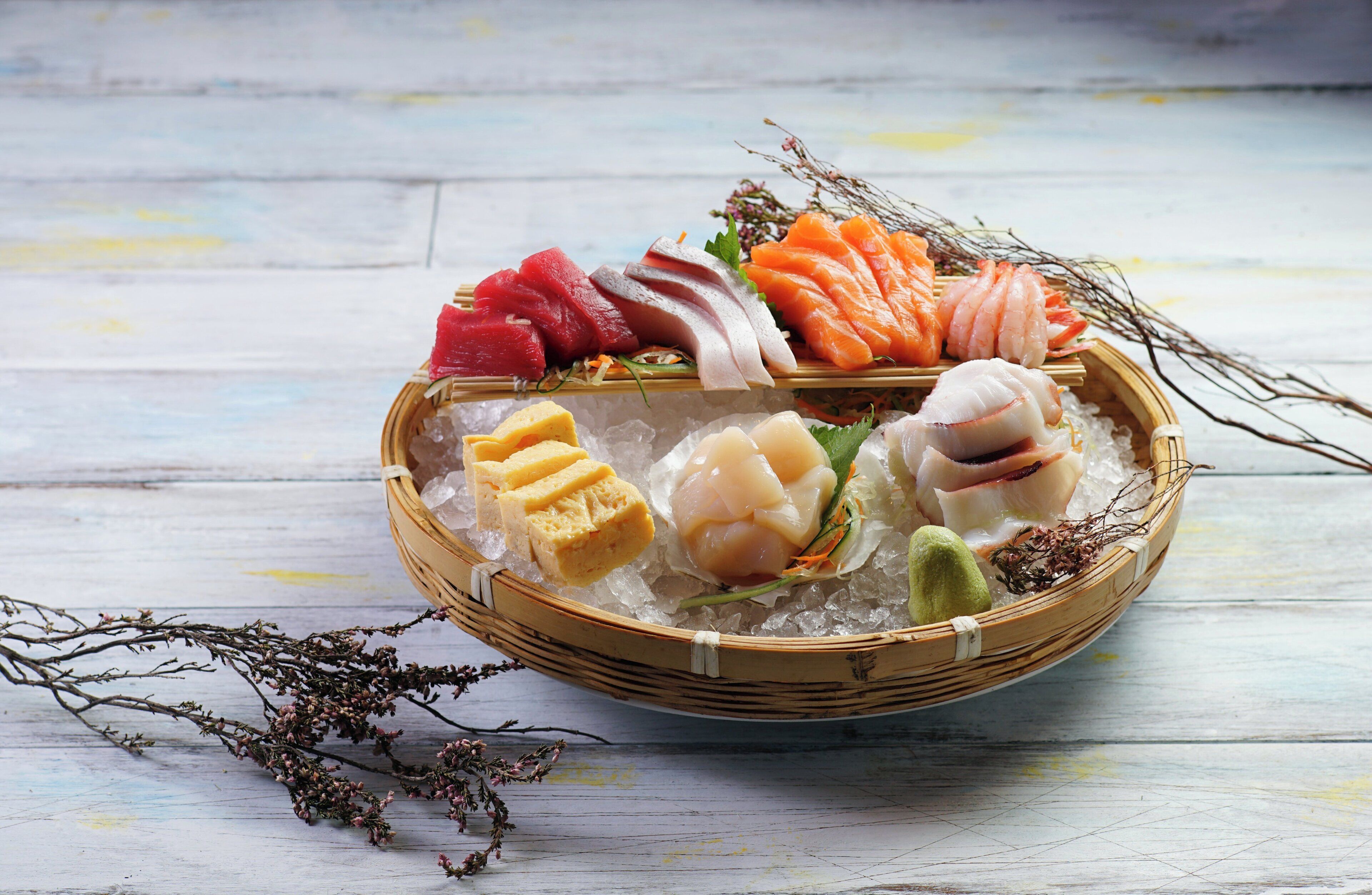 Un plato de sushi con diversos tipos de pescado y mariscos sobre hielo, adornado con hierbas y flores.