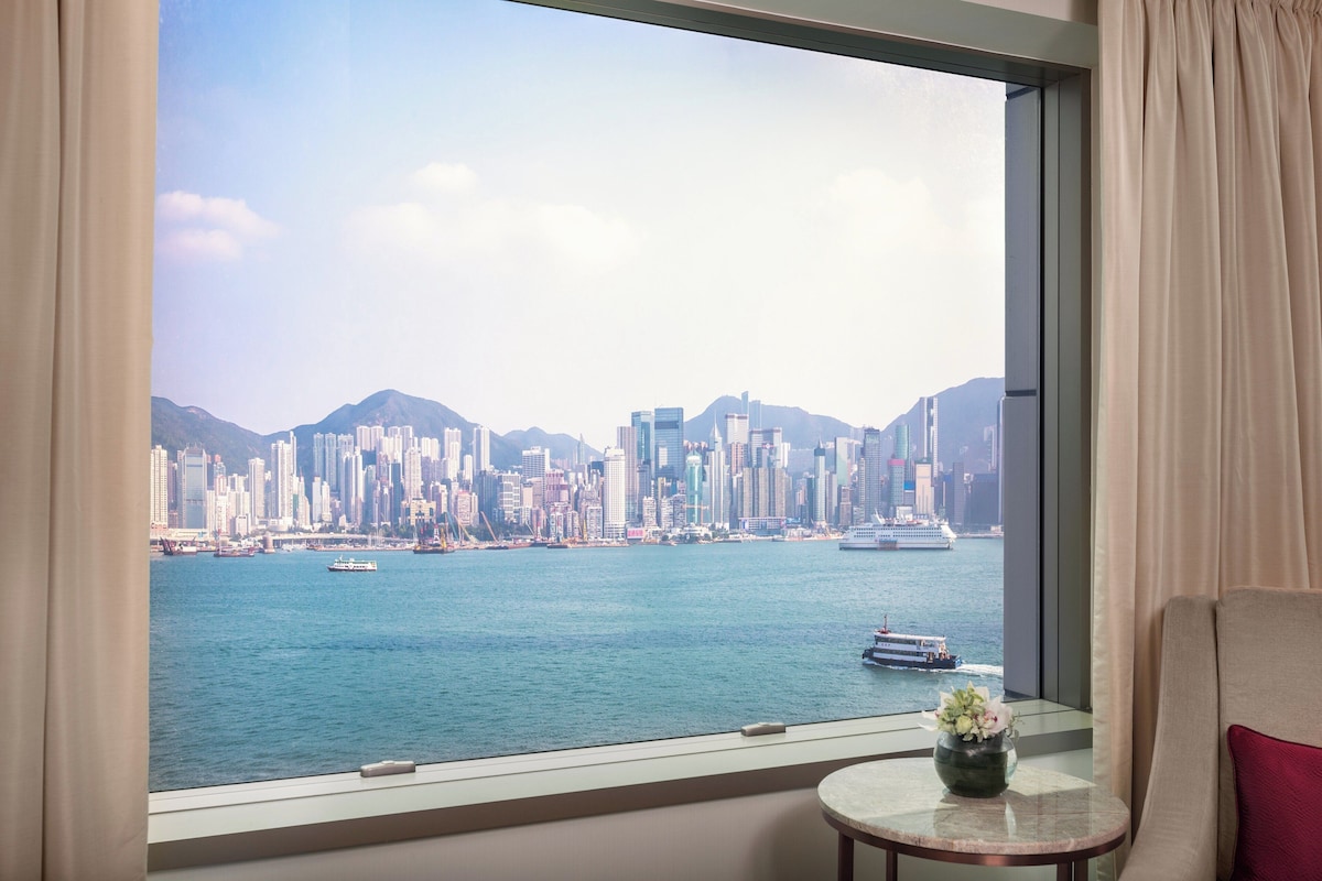 A room with a large window overlooking a city skyline and a body of water.