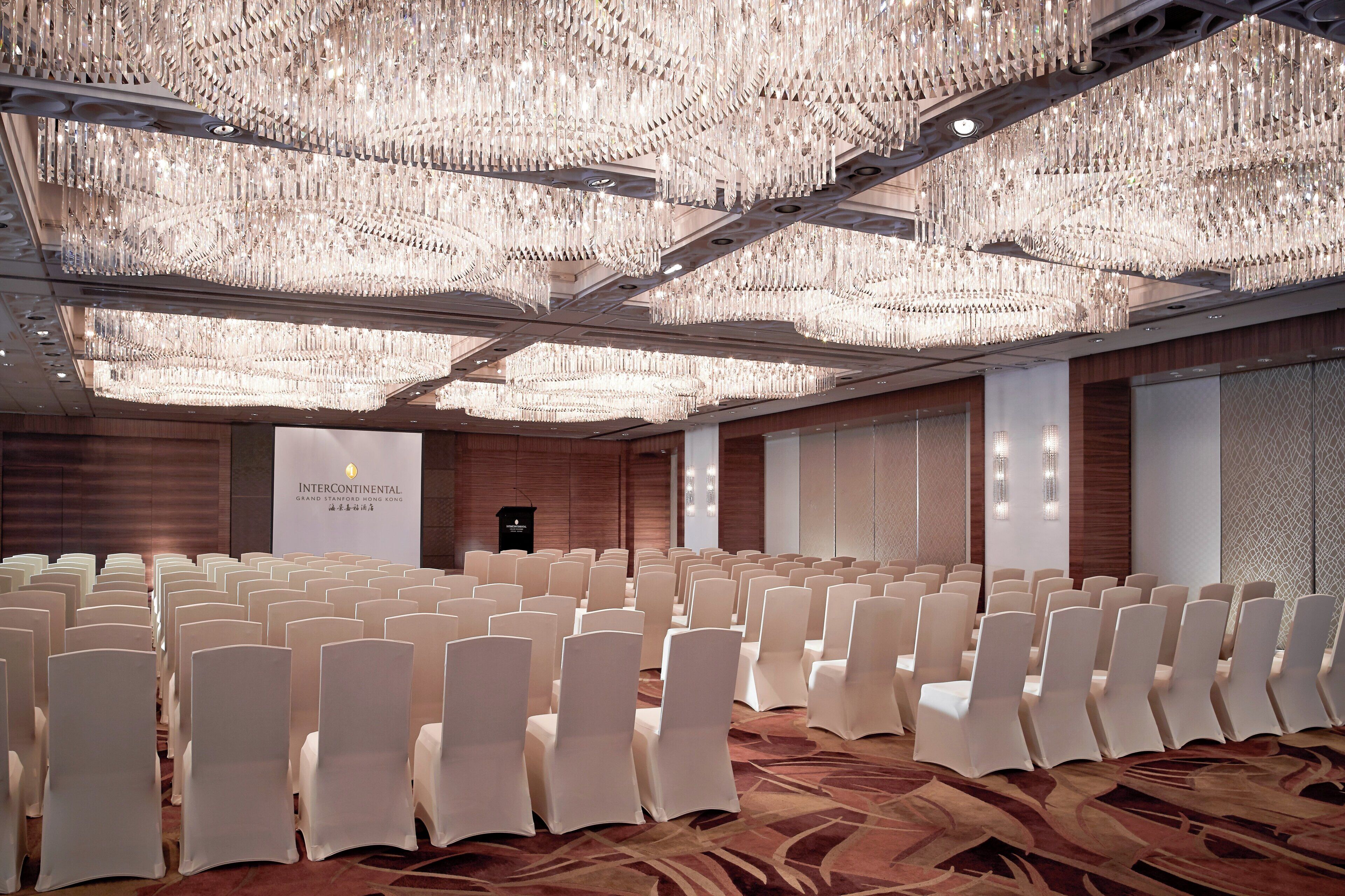 A conference room with rows of white chairs, a large chandelier, and a podium with a banner reading "Intercontinental Grand Stamford Hong Kong".