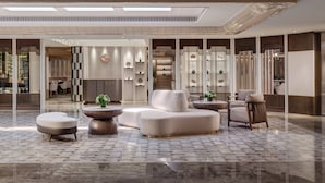 A spacious lobby with a modern design, featuring a large seating area with sofas and round tables, a reception desk, and a decorative wall with shelves. - InterContinental Grand Stanford Hong Kong by IHG (Kowloon)