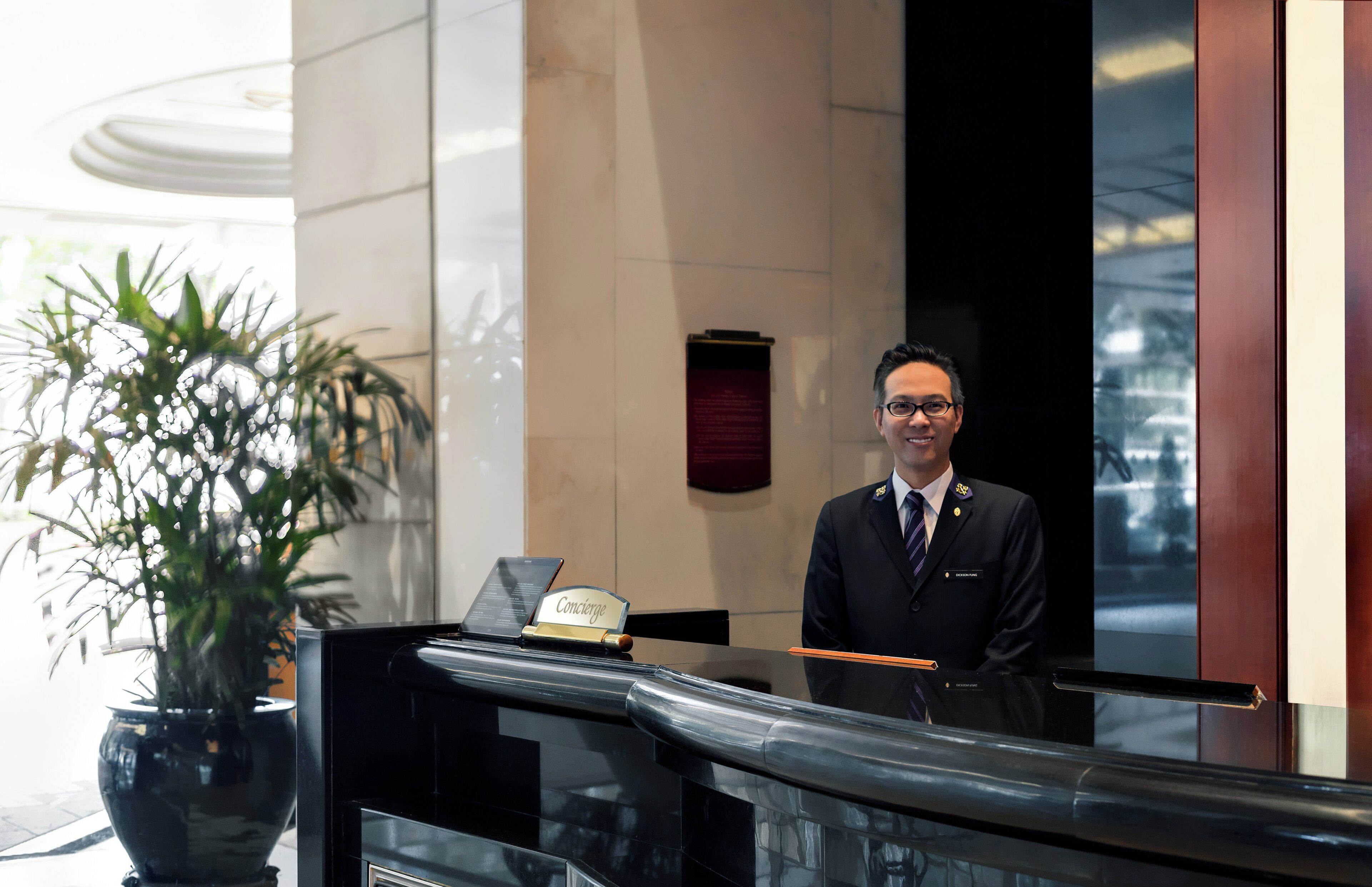 A hotel reception area with a concierge desk, a potted plant, and a sign indicating the concierge service.