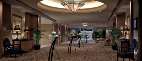 A hotel lobby with a patterned carpet, round tables, chairs, and a large chandelier.