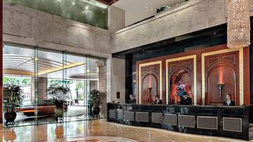 A spacious lobby with a marble floor, a reception desk, and a large chandelier.