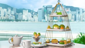 A tiered dessert stand with pastries and a teapot on a table with a city view in the background. - InterContinental Grand Stanford Hong Kong by IHG (Kowloon)