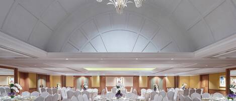 Un gran salón de banquetes con mesas redondas, sillas blancas y una lámpara central.