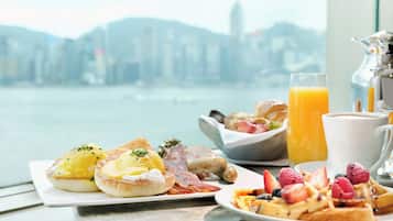 A breakfast table with eggs, bacon, sausages, waffles, and fruit, with a city view in the background.