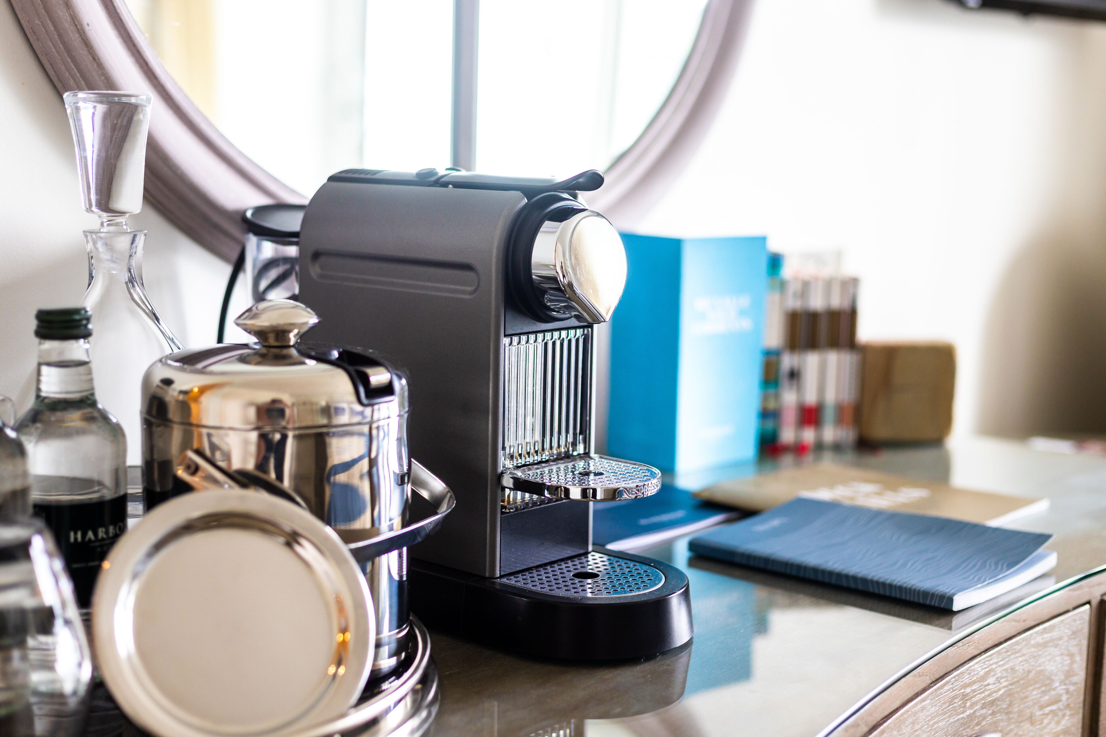 A coffee machine on a counter with a glass carafe, a metal pitcher, and a notebook.
