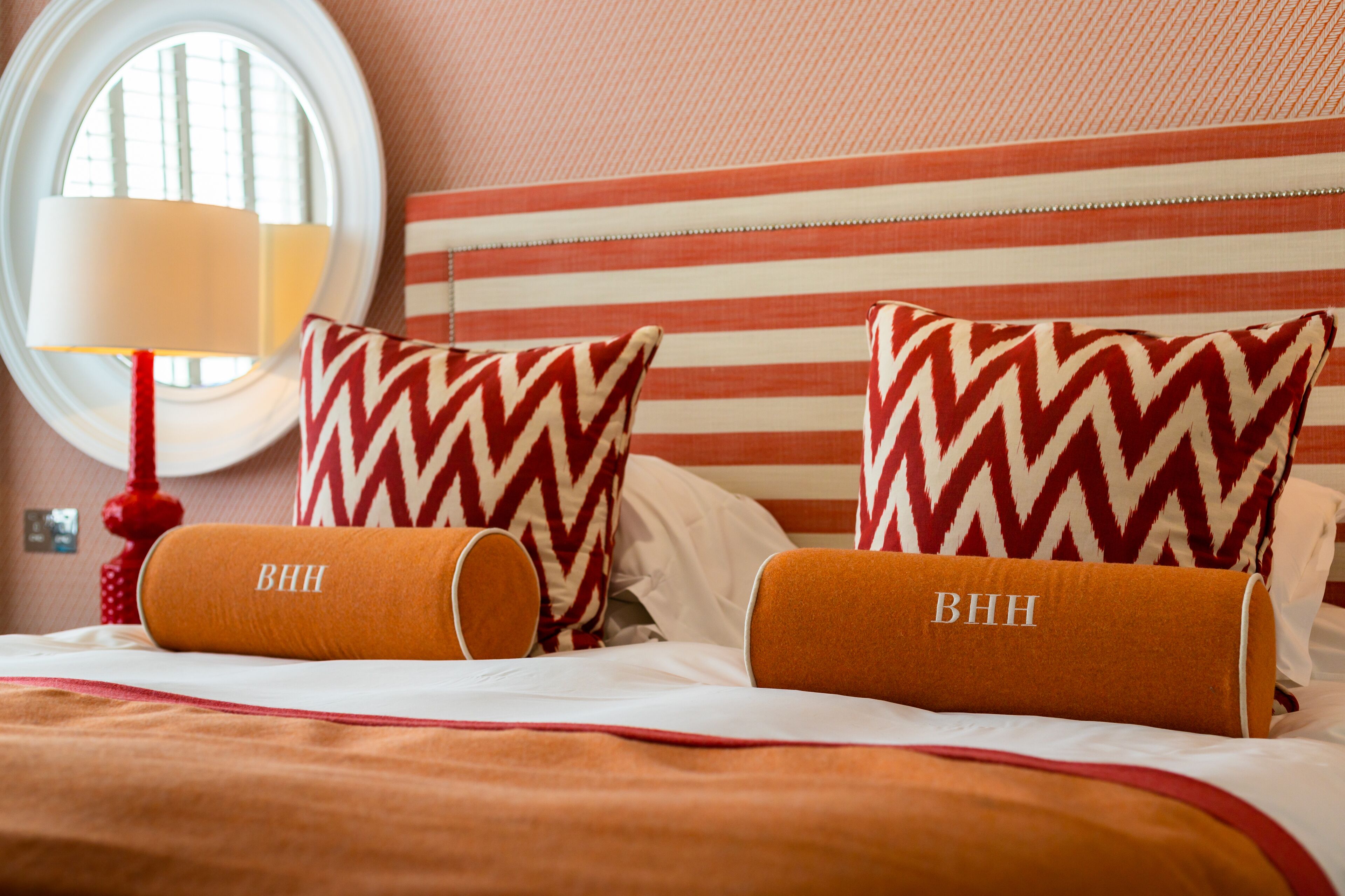 Ein Hotelzimmer mit Streifenmuster an den Wänden, zwei Kissen mit Zickzackmuster und einer roten Lampe.