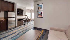Una habitació d'hotel moderna amb zona de cuina, sofà, escriptori i dos quadres penjats a la paret.