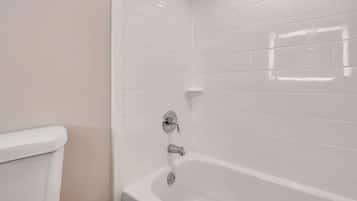 A bathroom with white tiled walls, a white bathtub, and a white toilet.