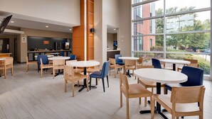 Una cafeteria moderna amb taules i cadires rodones, una zona de cuina i grans finestres que ofereixen vistes a l'exterior.