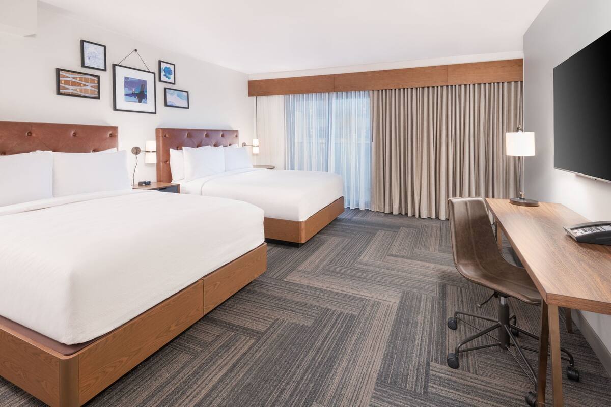 Habitación de hotel con dos camas, un escritorio y una televisión.