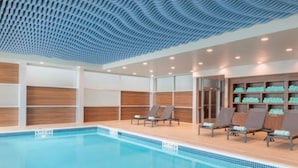 Una piscina interior con agua azul cristalina, rodeada de sillones de descanso y paneles de madera.