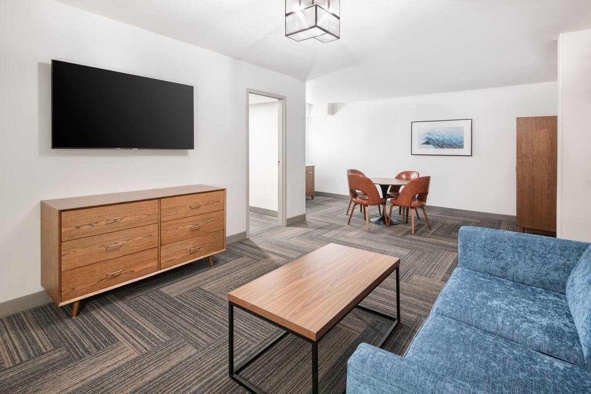 Una sala de estar moderna con un televisor de pantalla plana, un mueble de madera, un sofá azul y una pequeña mesa de madera.