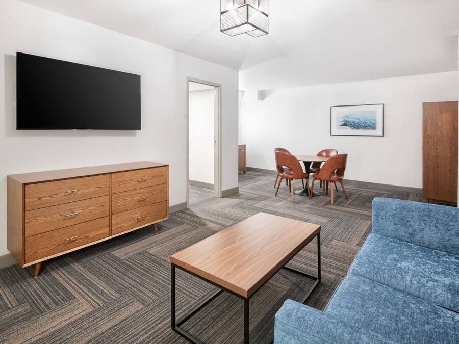 A modern living room with a flat-screen TV, wooden cabinet, blue sofa, and a small wooden table.