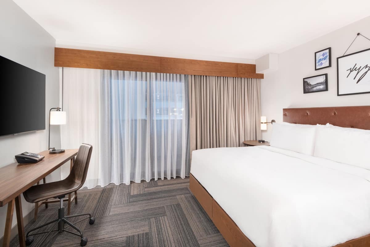 Una habitación de hotel con una cama grande, un escritorio con una silla, un televisor y cortinas.