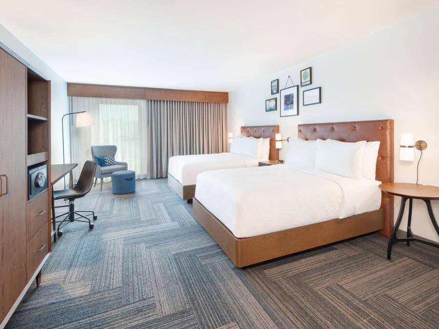 A hotel room with two beds, a desk, a chair, and a small table.
