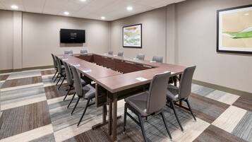 A conference room with a long table, chairs, a flat-screen TV, and framed artwork on the walls.