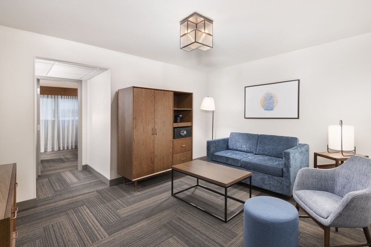 Une chambre d’hôtel moderne avec une armoire en bois, un canapé bleu, une table basse et une lampe.