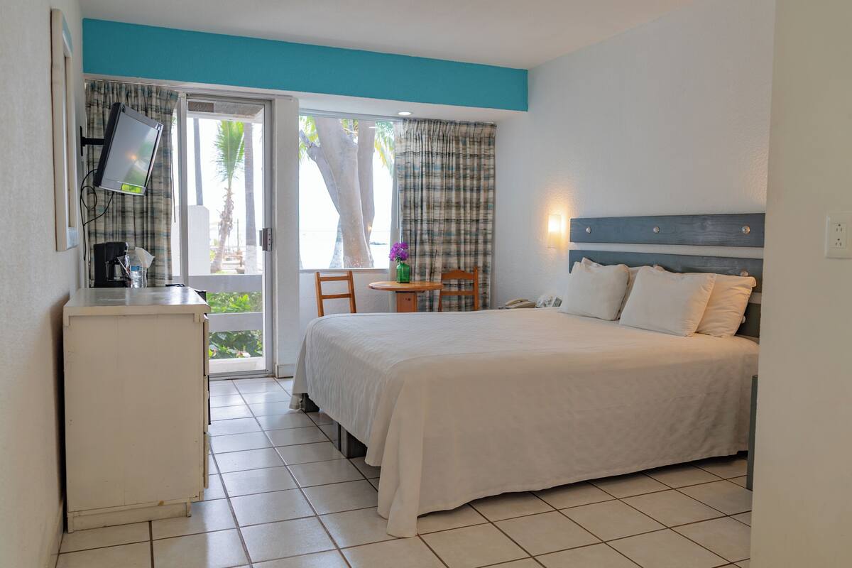 A hotel room with a bed, a desk, a chair, and a small table with a vase of flowers.