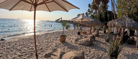 A beach with thatched umbrellas, lounge chairs, and a wooden table.