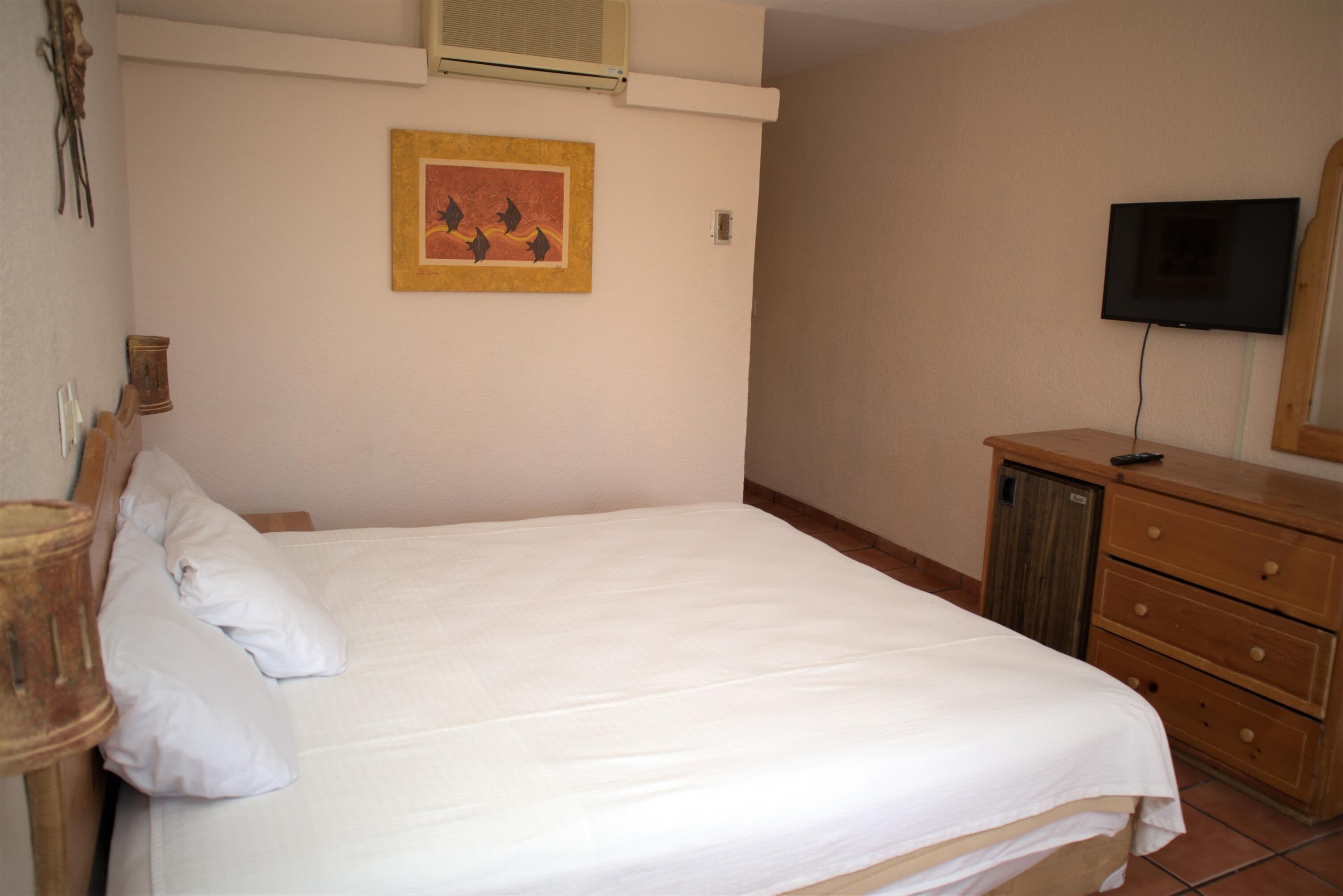 A bedroom with a bed, a dresser, a television, and a wall-mounted picture.