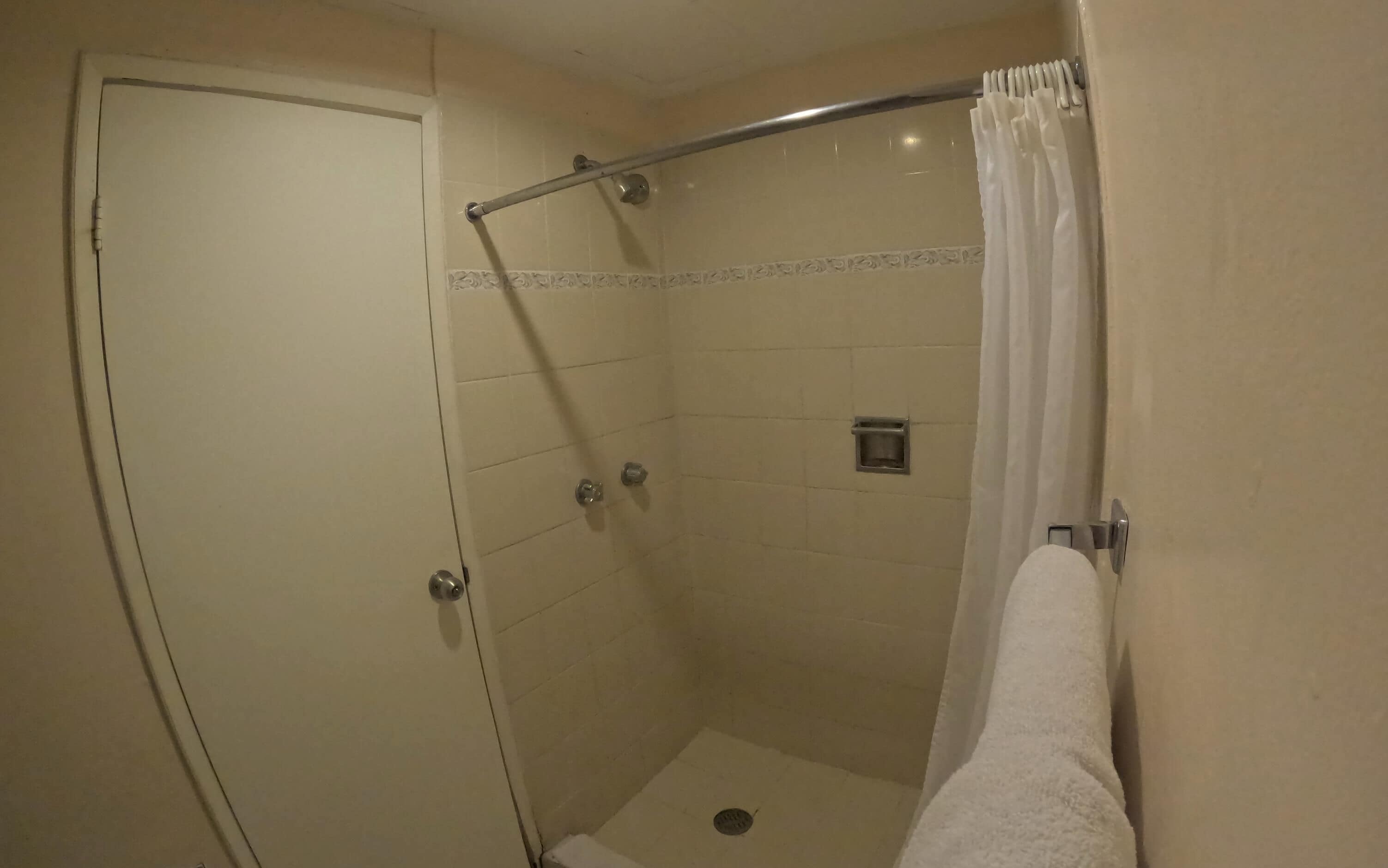 A small, enclosed shower area with a white shower curtain, a grab bar, and a single showerhead.