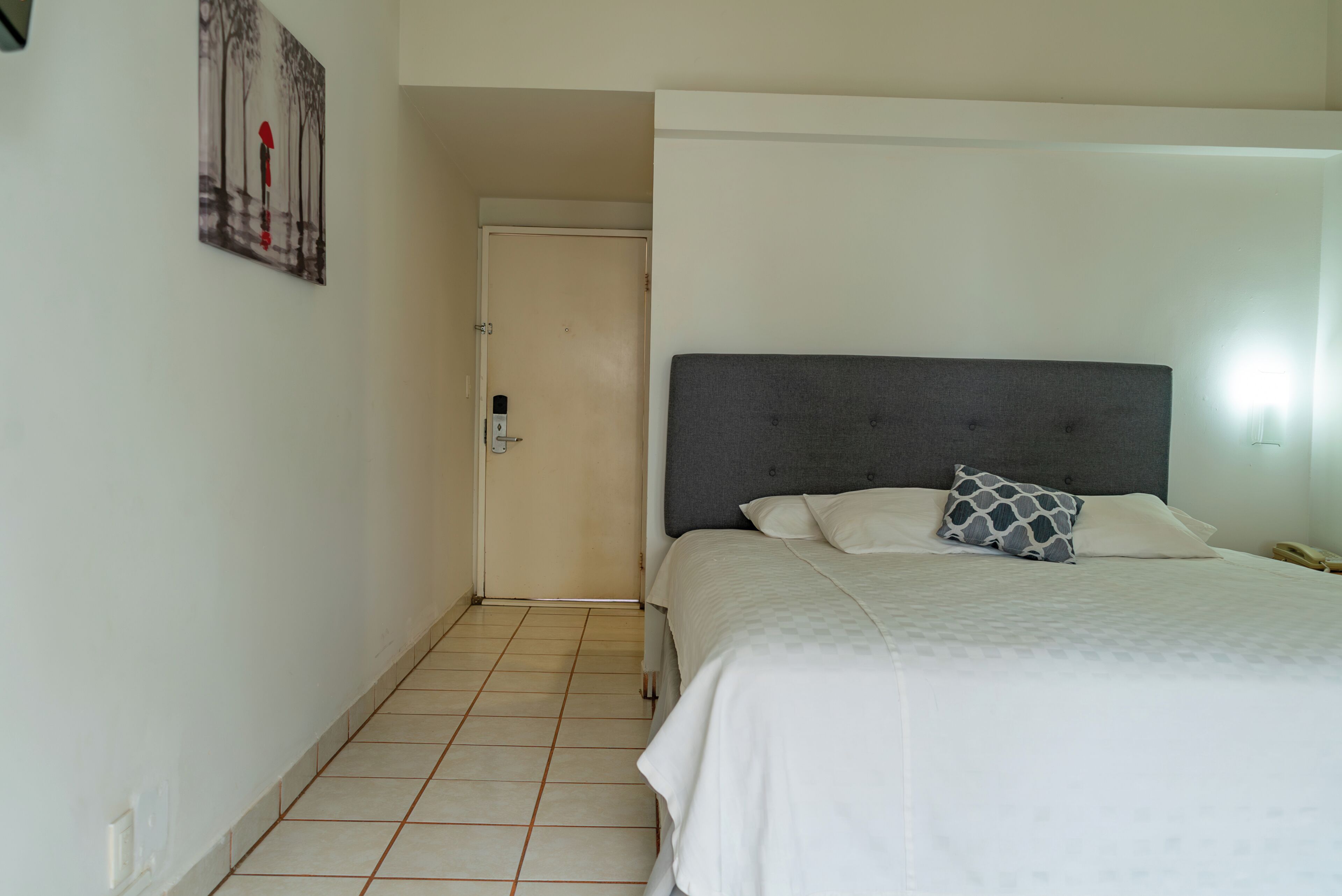 A hotel room with a bed, a door, a light fixture, and a tiled floor.