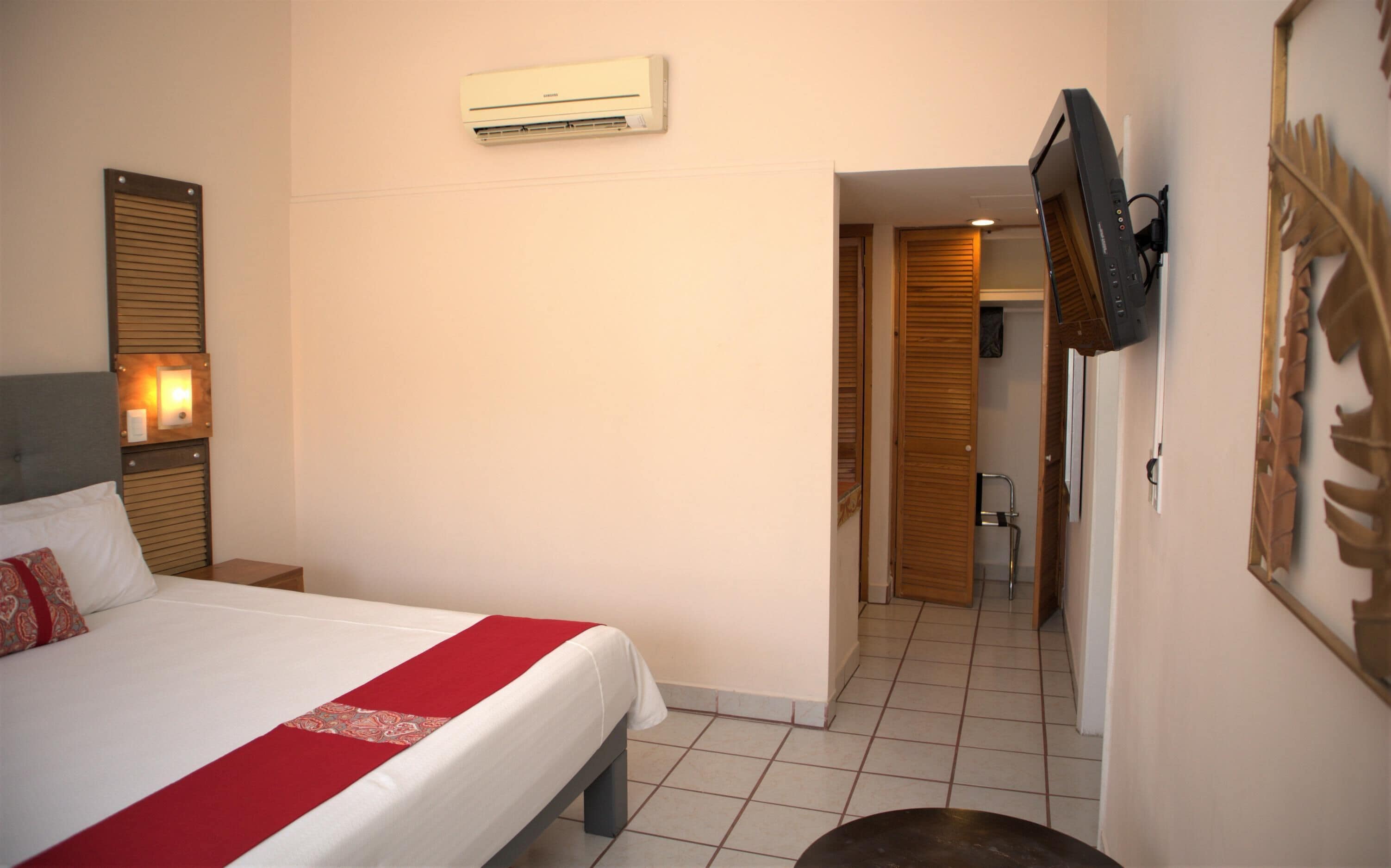 Ein Hotelzimmer mit einem Bett, einer Klimaanlage, einem an der Wand befestigten Fernseher und einem durch eine offene Tür einsehbarer Badezimmer.