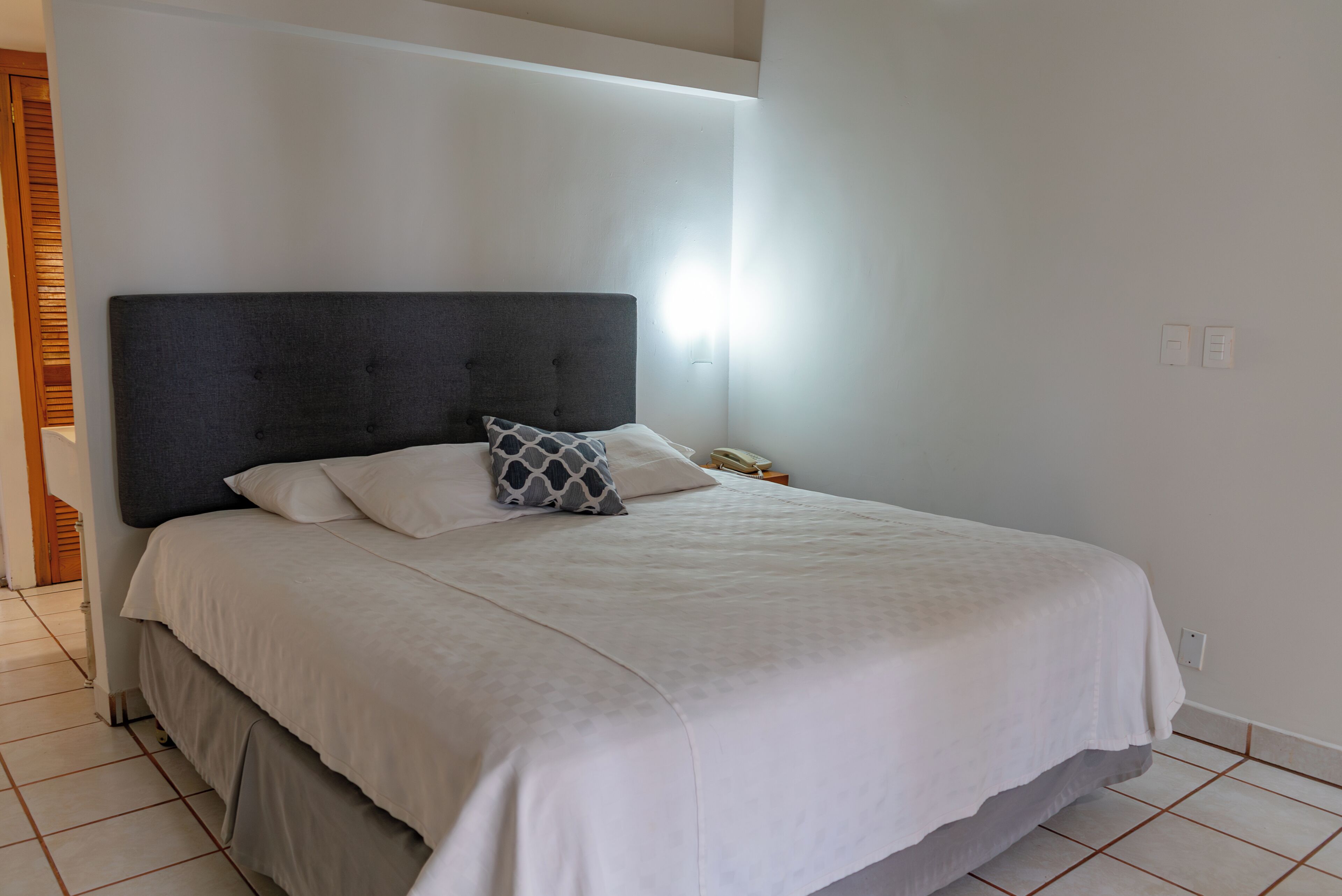 A neatly made bed with a dark headboard, white bedding, and a patterned pillow.