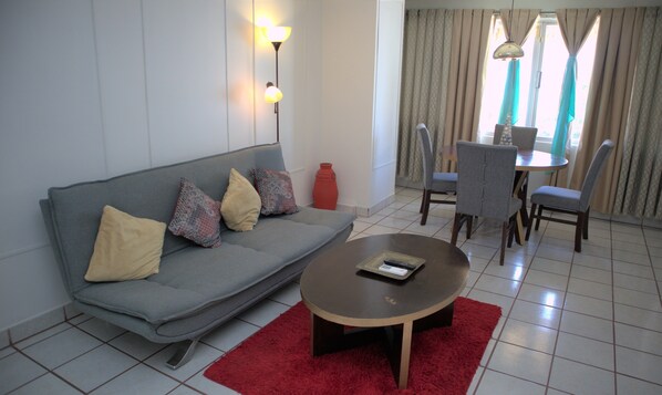 A living room with a grey sofa, red rug, and a small table with a remote control. - La Concha Beach Hotel & Club (La Paz)