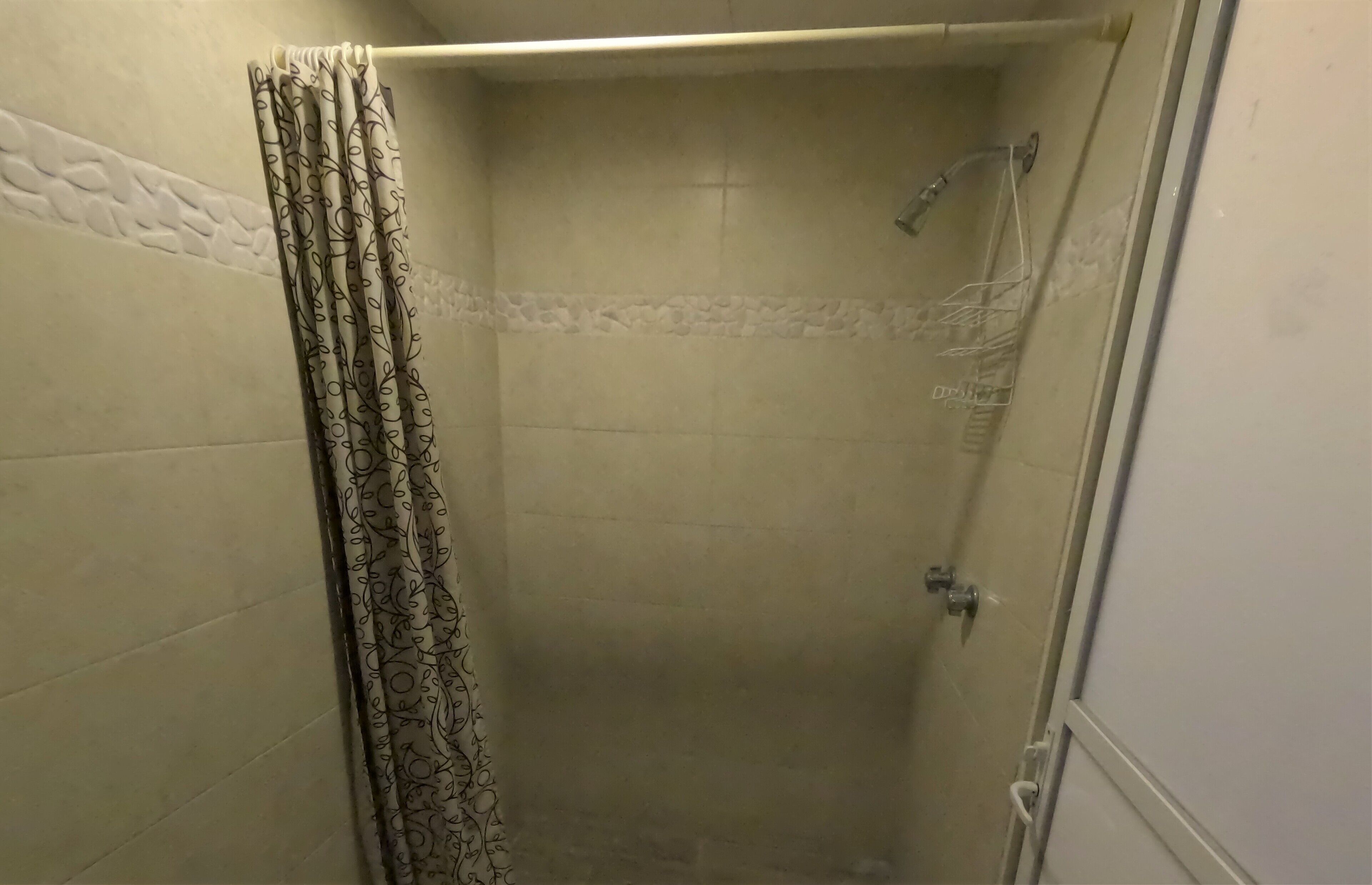 A bathroom with a shower, tiled walls, and a patterned curtain.