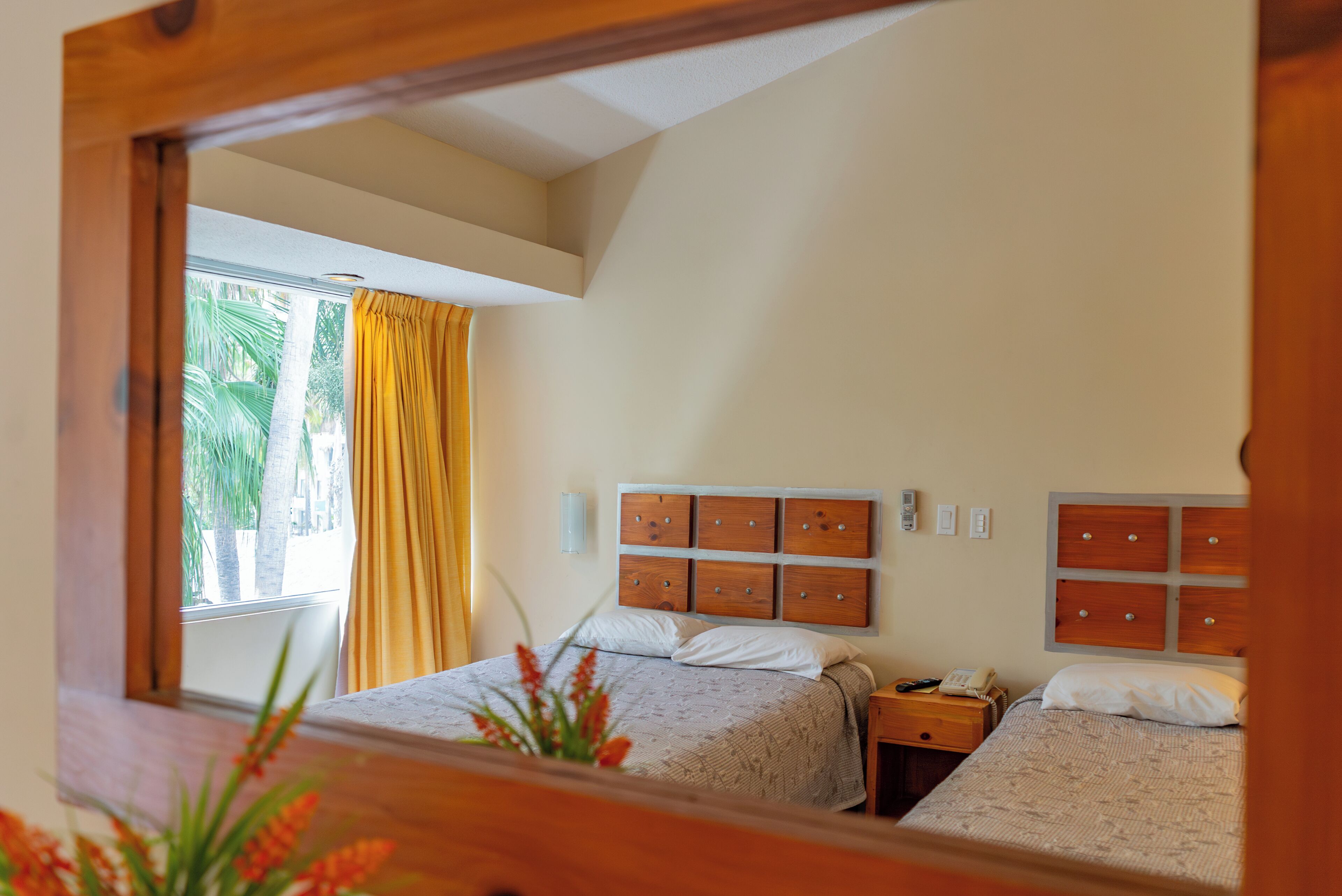Quarto com duas camas, cabeceira de madeira, mesa de cabeceira com telefone e janela com cortinas.
