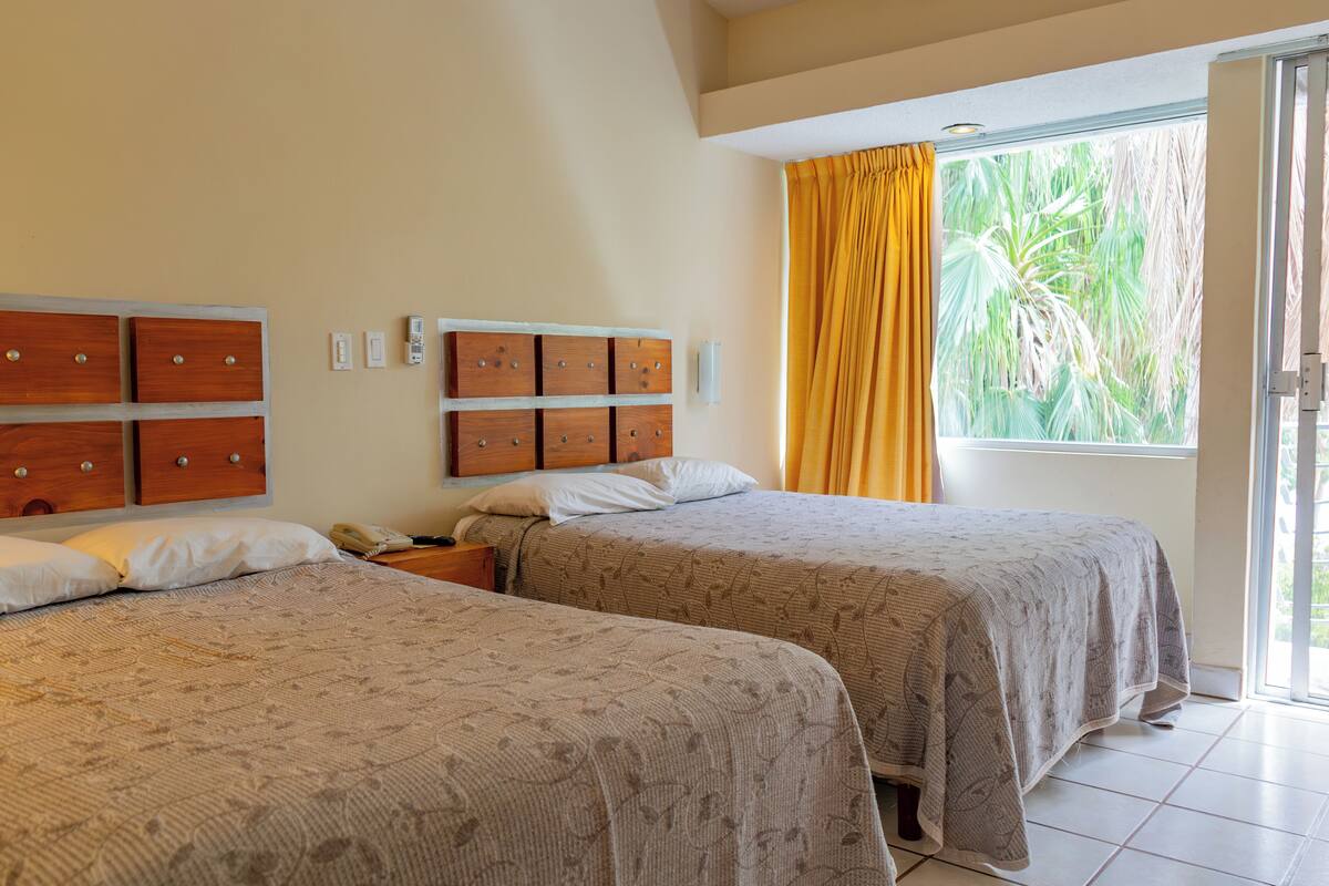 A hotel room with two beds, a wooden headboard, a nightstand, and a window with curtains.