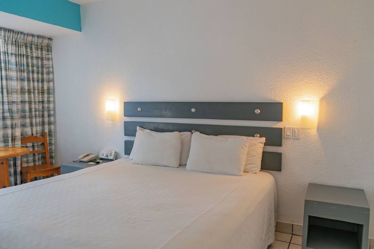A neatly made bed with a headboard, two bedside lamps, a telephone, and a small table with a chair.