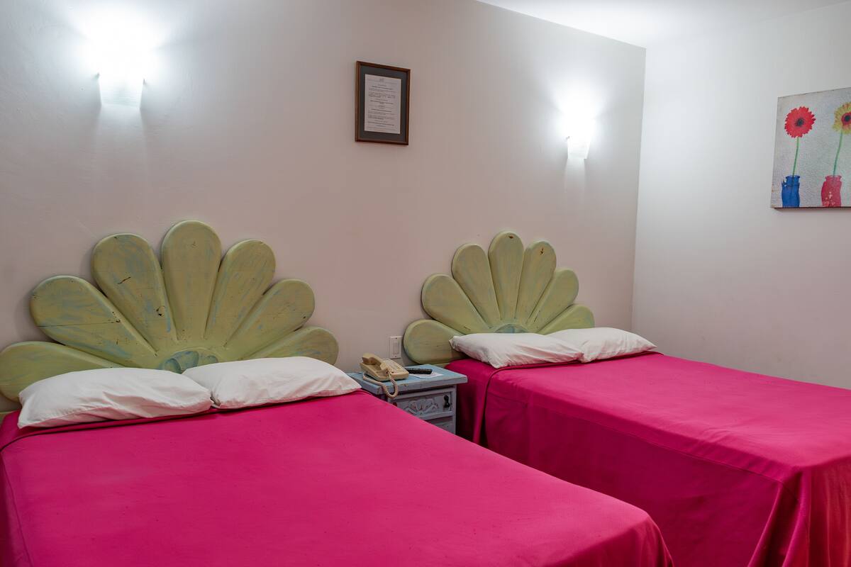 A room with two beds, each with a unique fan-shaped headboard, and pink bedding.