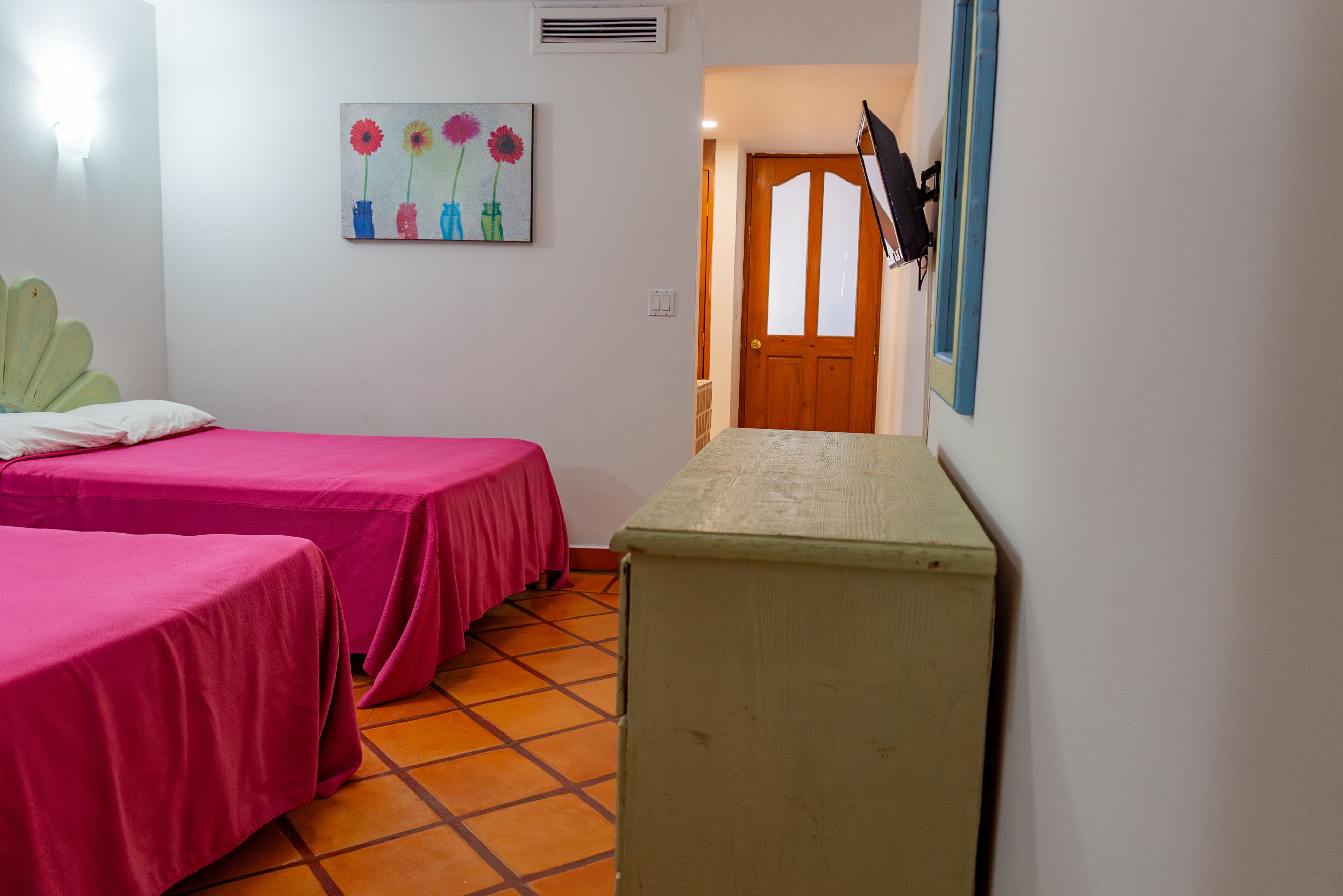 A hotel room with two beds, a painting, a door, and a small table.
