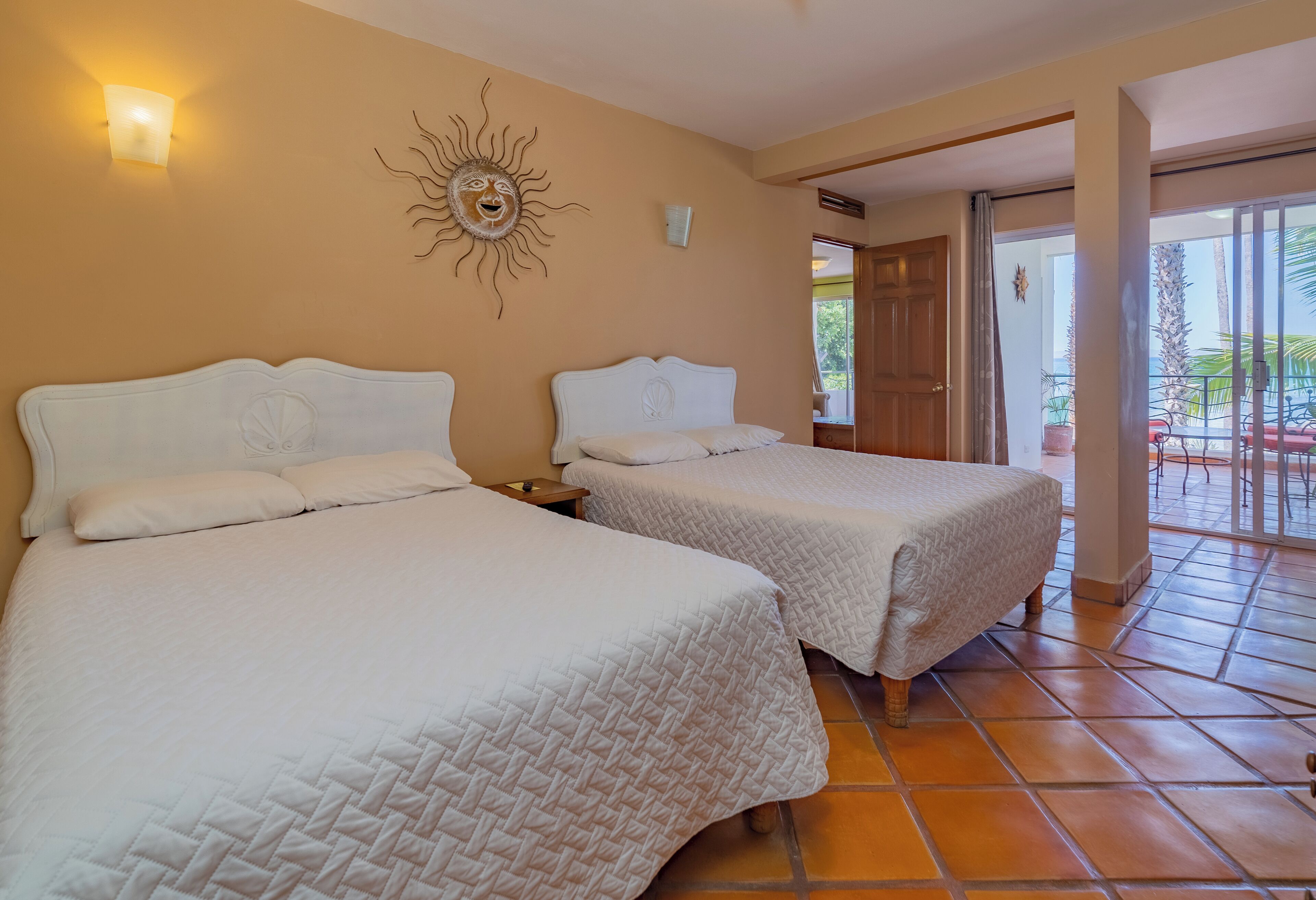 A hotel room with two beds, a sun decoration on the wall, and a view of the outdoor area.