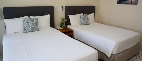 Zwei Einzelbetten mit weißen Bettwäsche und dunklen Kopfteilen in einem Hotelzimmer.