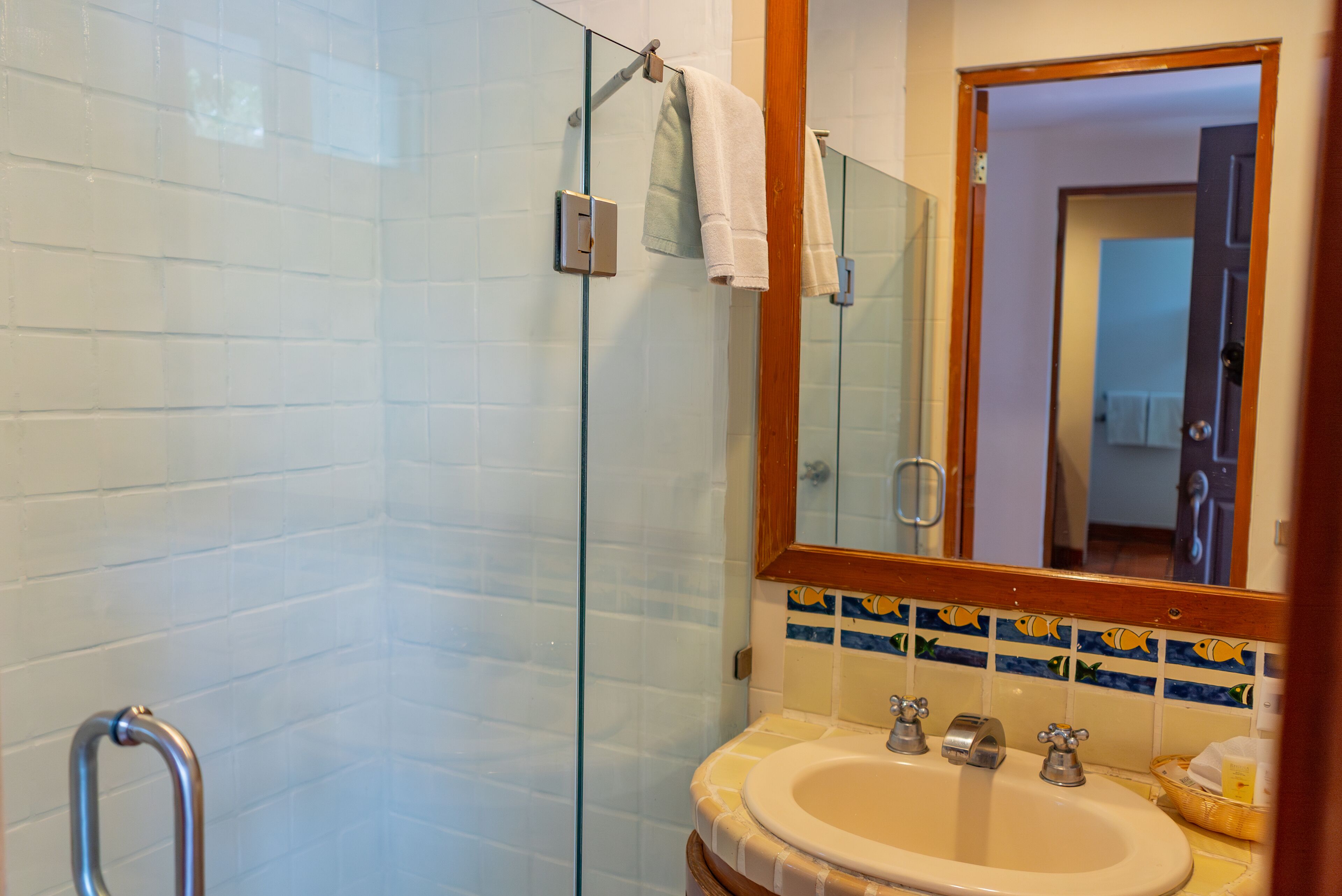 Un baño con cabina de ducha de vidrio, un lavabo doble y un espejo con marco de madera.