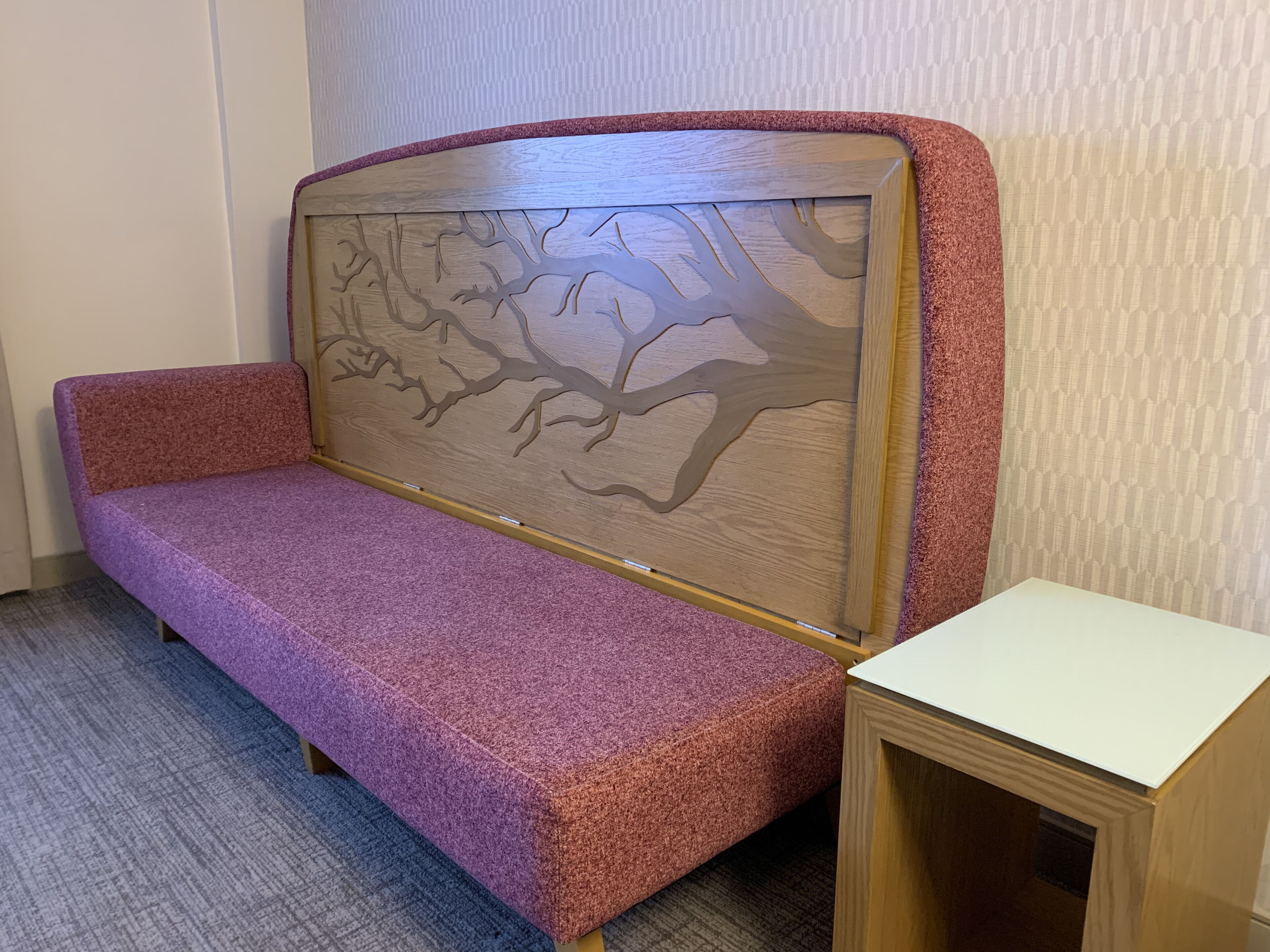 A room with a purple sofa, a small wooden table, and a patterned wall.